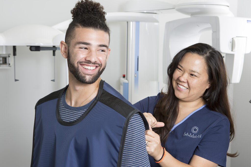 Smiling patient at Canales Orthodontics in Gardendale and Alabaster, AL, smiling with x-ray vest on and orthodontic assistant preparing smile scan for Dentofacial Orthopedics