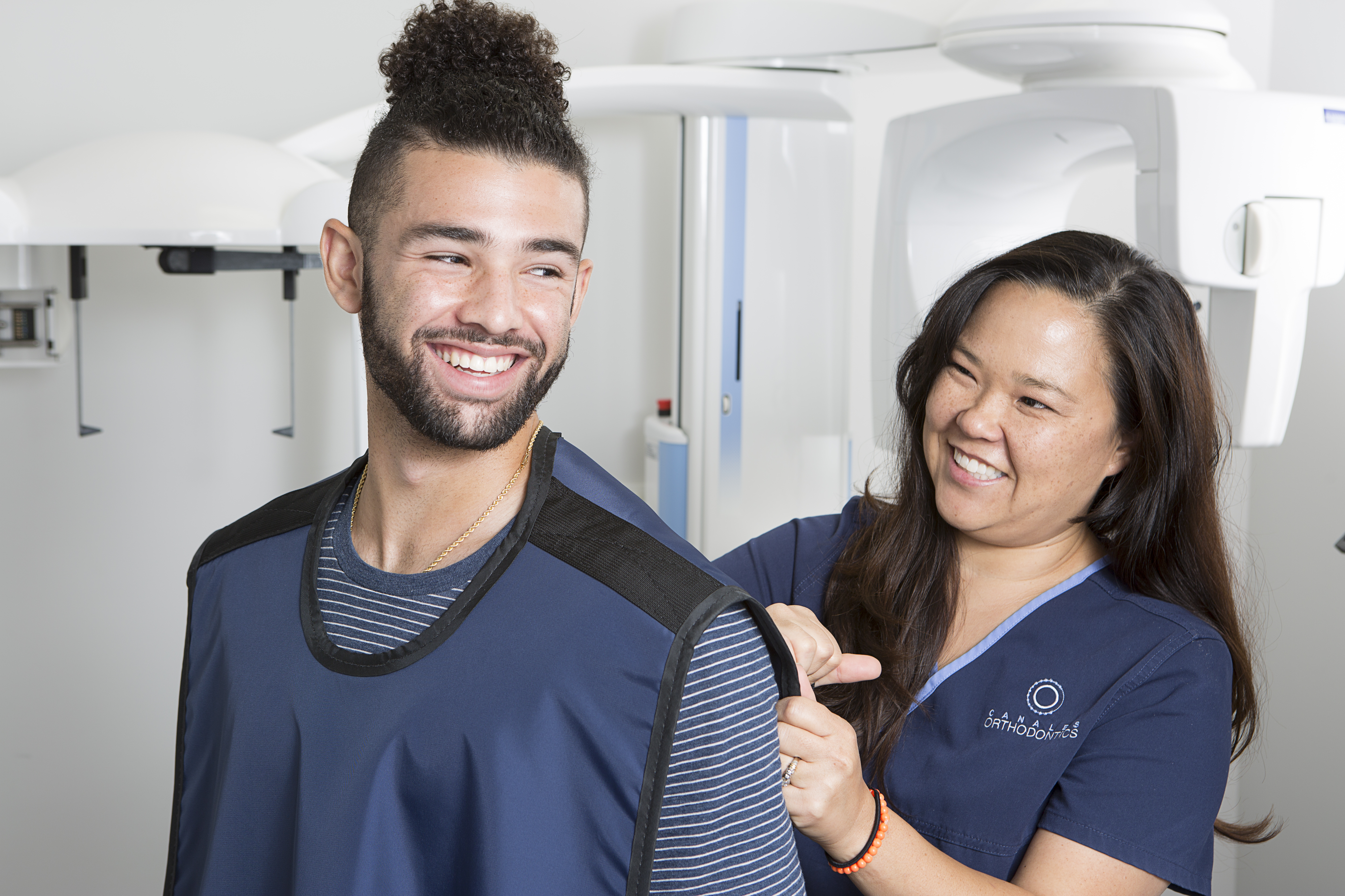Smiling patient at Canales Orthodontics in Gardendale and Alabaster, AL, smiling with x-ray vest on and orthodontic assistant preparing smile scan for Dentofacial Orthopedics